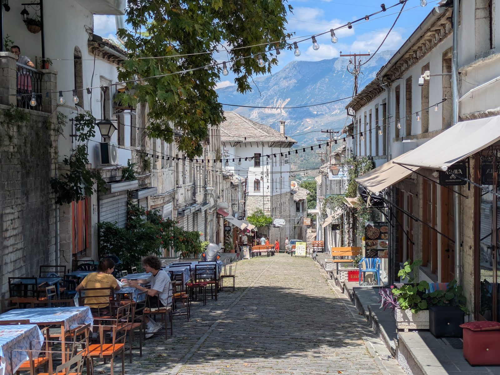 Terrazas con mesas en una calle empedrada del casco antiguo de Gjirokastra, con las montañas al fondo