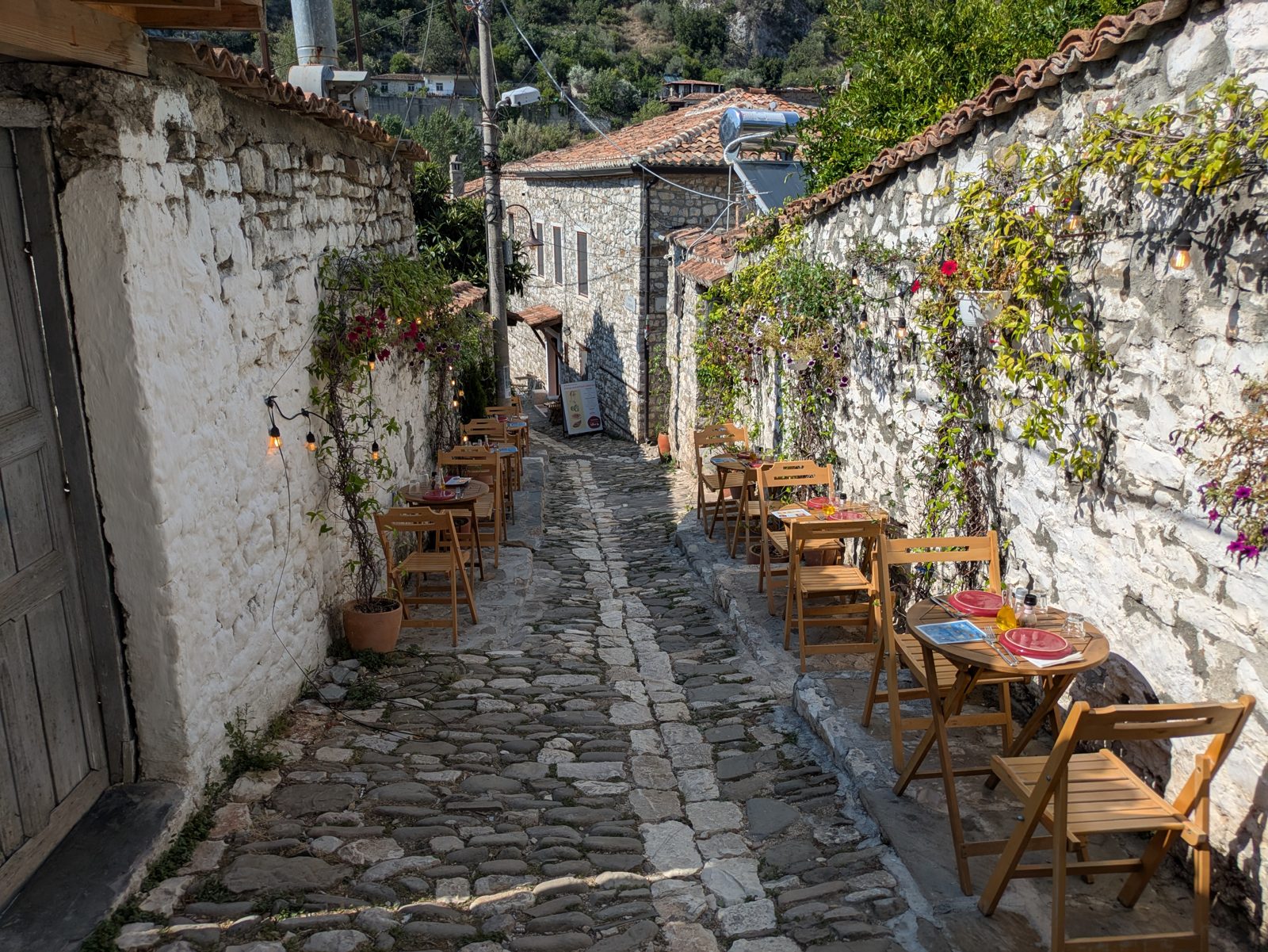 Callejón empedrado del barrio de Gorica con mesas de terraza junto a un muro de piedra