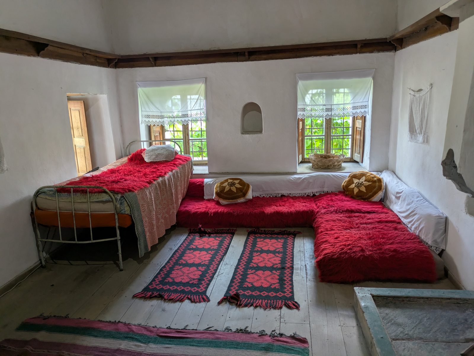 Sala de la Casa Skënduli con divanes rojos, cojines y alfombras junto a las ventanas