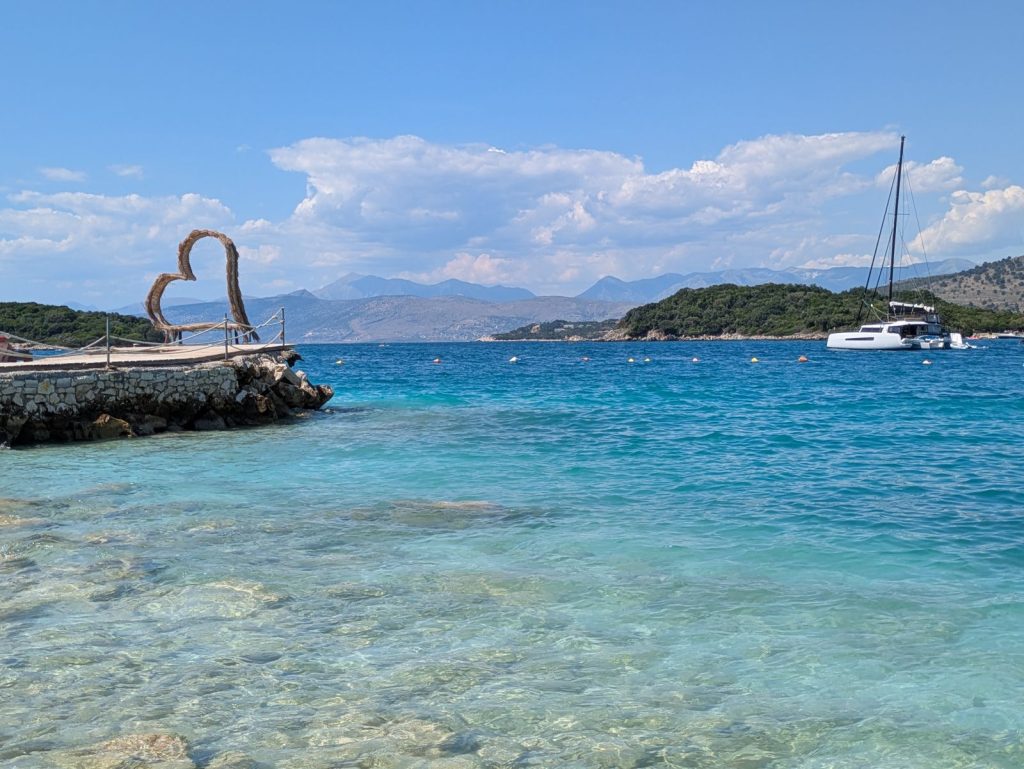 Agua cristalina en una playa de Ksamil con uno de los islotes y un velero al fondo