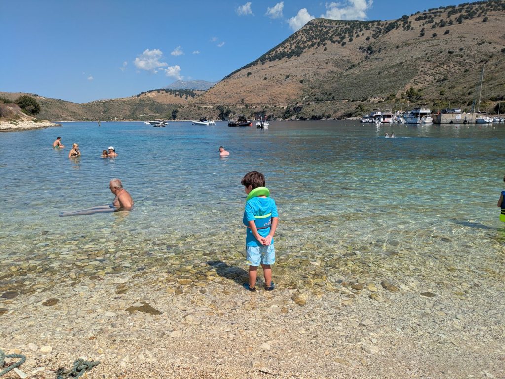 Ares de espaldas en el agua transparente de la bahía de Porto Palermo, con las montañas al fondo